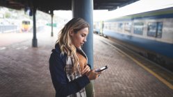 Вид збоку вагітної жінки, що використовує мобільний телефон на залізничній станції — стокове фото