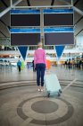 Rear view of female commuter standing with luggage at waiting area in airport — Stock Photo