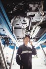 Жінка-механік розмовляє на мобільному телефоні під машиною в ремонтному гаражі — стокове фото