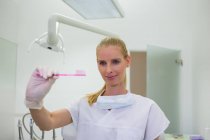 Une dentiste tenant une brosse à dents rose à la clinique — Photo de stock