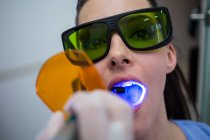 Dentista examinando os dentes do paciente com luz de cura dentária na clínica, close-up — Fotografia de Stock