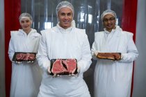 Retrato de açougueiros mostrando bandejas de carne na fábrica de carne — Fotografia de Stock