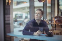 Pensativo ejecutivo masculino sosteniendo el teléfono móvil en la cafetería - foto de stock