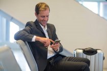 Smiling businessman using mobile phone in waiting area at airport terminal — Stock Photo