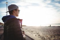 Задумчивый человек с чашкой кофе наслаждается природой на пляже — стоковое фото