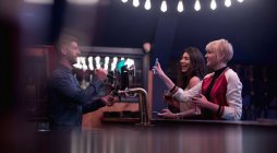 Barman interagindo com mulheres bonitas no balcão no bar — Fotografia de Stock