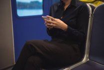 Sección media de la mujer de negocios usando el teléfono mientras está sentada en el tren - foto de stock