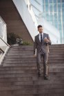 Uomo d'affari che utilizza il telefono cellulare mentre cammina lungo i gradini — Foto stock
