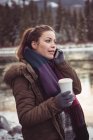 Жінка стоїть на березі річки і використовує мобільний телефон взимку — стокове фото