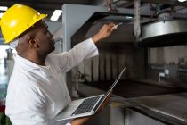 Männlicher Arbeiter trägt Laborkittel, während er Laptop in Saftfabrik benutzt — Stockfoto