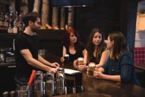 Друзья, держащие пивные бокалы за стойкой бара и общающиеся с барменом — стоковое фото