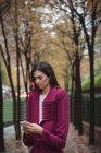 Geschäftsfrau benutzt Handy, das auf Gehweg mit Bäumen steht — Stockfoto