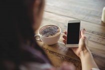 Женщина держит мобильный телефон в кафе — стоковое фото