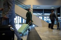 Business people walking with luggage in waiting area at airport — Stock Photo