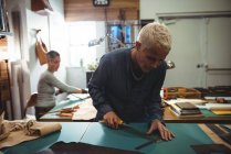 Внимательная ремесленница режет кожу в мастерской — стоковое фото