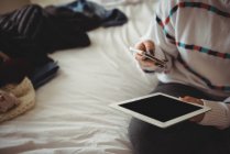 Женщина сидит на кровати с помощью мобильного телефона и цифрового планшета в спальне — стоковое фото