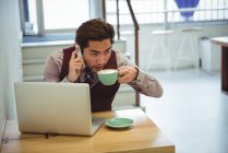 Чоловік розмовляє по мобільному телефону, маючи каву в кав'ярні — стокове фото