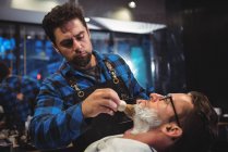 Barbier appliquer de la crème sur la barbe du client dans le salon de coiffure — Photo de stock