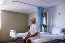 Paciente mayor masculino reflexivo sentado en la sala del hospital - foto de stock