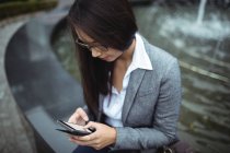 Крупный план деловой женщины, сидящей возле фонтана и пользующейся мобильным телефоном — стоковое фото