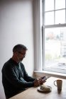 Mann sitzt am Tisch und benutzt Handy zu Hause — Stockfoto