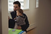 Father holding his baby while using digital tablet at desk in home — Stock Photo