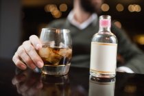 Мужская рука со стаканом напитка и небольшим ликером на столе в баре — стоковое фото