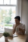 Homem olhando para laptop enquanto toma uma xícara de café em casa — Fotografia de Stock