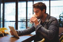 Чоловік використовує цифровий планшет, маючи каву в кафе — стокове фото