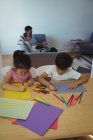 Мальчик и девочка рисуют бумагой, в то время как родители используют ноутбук в фоновом режиме дома — стоковое фото