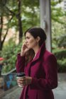 Seitenansicht einer Geschäftsfrau, die Einweg-Kaffeetasse in der Hand hält und mit dem Handy spricht — Stockfoto