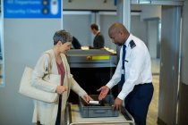 Oficial de seguridad del aeropuerto verificando el teléfono móvil del viajero en la terminal del aeropuerto - foto de stock
