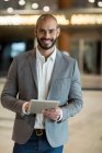 Портрет улыбающегося бизнесмена с цифровым планшетом в зоне ожидания в терминале аэропорта — стоковое фото