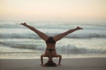 Donna che esegue headstand sulla spiaggia al crepuscolo — Foto stock