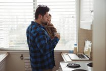 Father having coffee while holding baby boy in kitchen — Stock Photo
