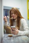 Красивая женщина с помощью мобильного телефона во время еды салат в кафе — стоковое фото