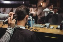 Hombre consiguiendo pelo recortado por estilista con trimmer en peluquería - foto de stock