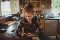 Lächelnde Frau benutzt Handy in der heimischen Küche — Stockfoto