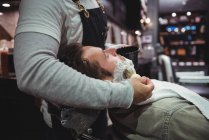 Metà sezione di barbiere che applica la crema a barba di cliente in negozio di barbiere — Foto stock
