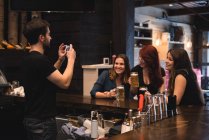 Bartender tirar fotos de mulheres no balcão de bar usando telefone celular — Fotografia de Stock