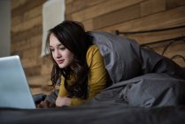 Женщина лежит на кровати с помощью ноутбука в спальне дома — стоковое фото