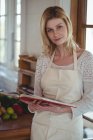 Retrato de mujer hermosa sosteniendo libro de recetas en la cocina en casa - foto de stock
