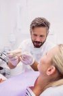 Dentist showing denture model to female patient in clinic — Stock Photo