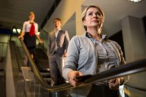 Businesswoman with boarding pass on escalator in airport — Stock Photo