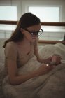 Жінка тримає чашку і використовує мобільний телефон в ліжку вдома — стокове фото