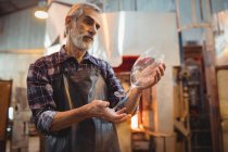 Glassblower examining glassware at glassblowing factory — Stock Photo
