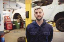 Retrato de jovem mecânico em pé na garagem de reparação — Fotografia de Stock