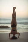 Woman performing headstand on beach at dusk — Stock Photo