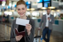 Портрет усміхненої бізнес-леді, що показує свій посадковий талон в терміналі аеропорту — стокове фото
