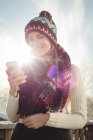Усміхнена жінка в зимовому вбранні вводить текстове повідомлення проти яскравого сонячного світла — стокове фото